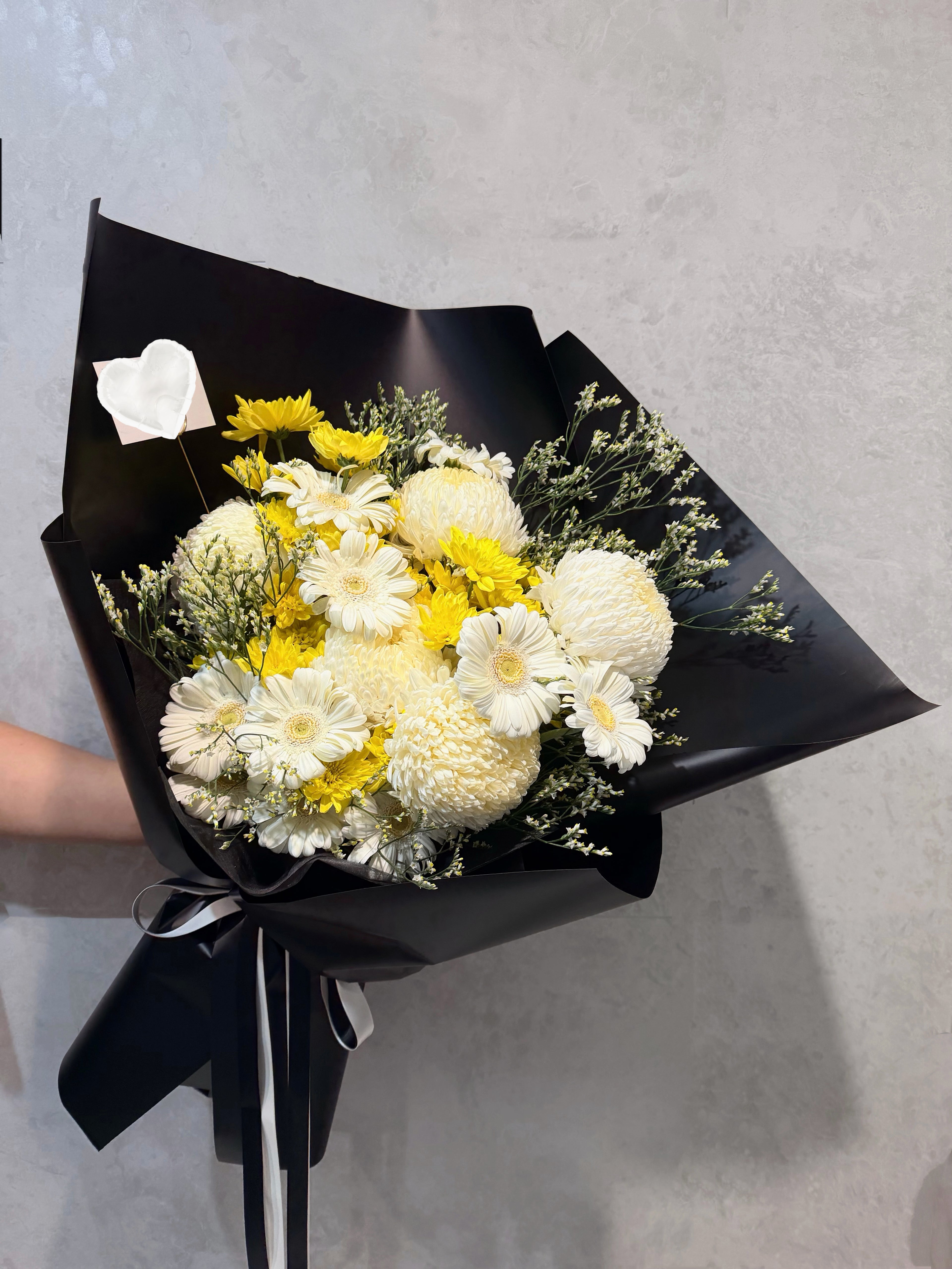 White and pale yellow sympathy bouquet wrapped in black